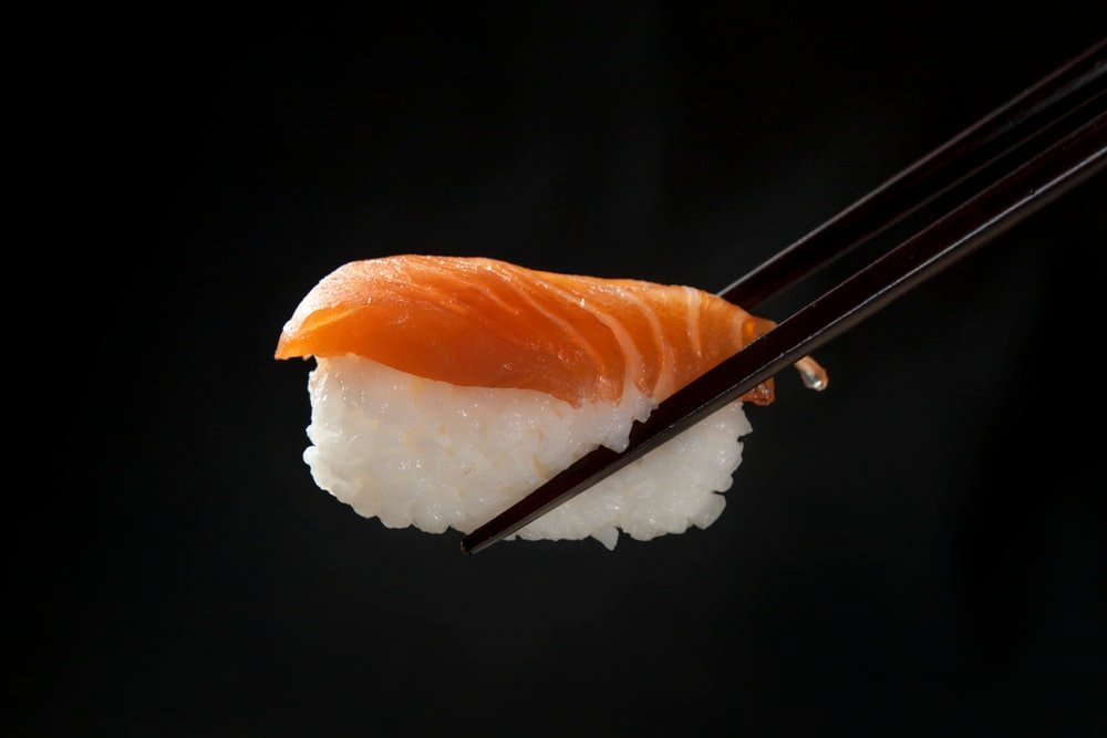 Salmon nigiri held with chopsticks against a dark background